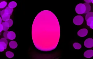 Defocused Prints: Shining Hot Pink Egg Shaped Table Lamp with Purple Bokeh Light on Dark Background