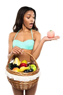 Surprised Prints: shocked african american woman with basket of fruits holding peach, isolated on white