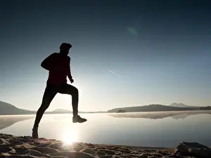 Sunrise Beach Prints: Silhouette of athletic runner jogging on the beach against orange sunrise