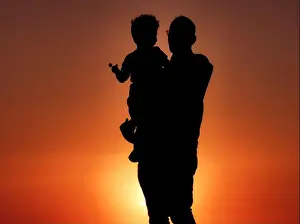 Back Lit Prints: A silhouette of a grandfather holding his grandson with a lollipop at sunset on the coast of Cape Zebib