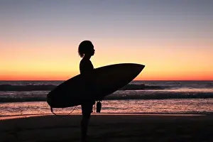 Silhouette of Oniel Lopez, young male surfer holding his surfboard at sunset on Jiquilillo beach, Nicaragua