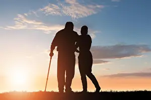 Assist Prints: Silhouette Of Woman Assisting Her Disabled Father Walking In Park At Dusk