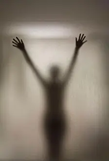 Behind Prints: Silhouette of a woman posing behind the glass door of a shower stall in a hotel room