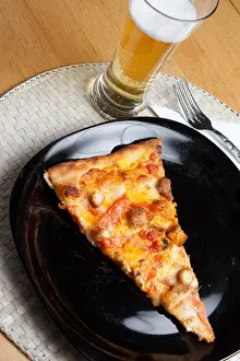 Supper Prints: A single slice of buffalo chicken pizza and a glass of light beer. Shallow depth of field