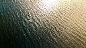 A small boat rests on the rippling waters of a lake in Finnish Lapland, bathed in the warm glow of the setting sun