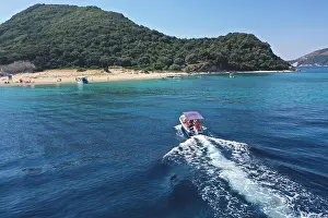 Small boat with tourists heading to iconic small uninhabited island of Marathonisi featuring clear water sandy shore and natural hatchery of Caretta-C