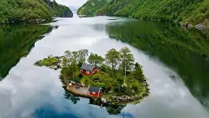 Green Forest Prints: A small island with two red cabins nestled among green trees is surrounded by calm