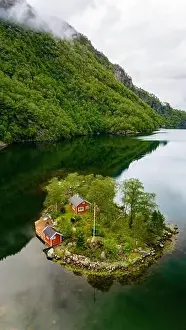 Lovrafjorden Prints: A small island with two red cabins nestled amongst lush greenery sits peacefully in a Norwegian fjord