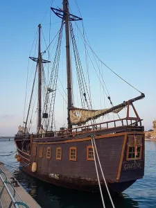 Boating Prints: Small old wooden pirate ship with old mast and sails in Gandia harbor in Spain under blue evening sky
