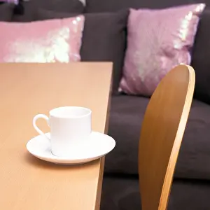 Insomnia Prints: One small white cup on an edge of a table with light timber ergonomic dining chair