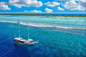 Small yacht sailing in tropical sea over coral reef in Indian ocean lagoon. Exotic island landscape, aerial view, tranquil nature scenic