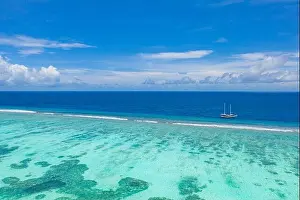 Small yacht sailing in tropical sea over coral reef in Indian ocean lagoon. Exotic island landscape, aerial view, tranquil nature scenic
