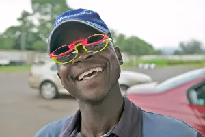 Color Photography Prints: Smiling African man a gas station attendant wears 2 sets of colored sun glasses South Africa