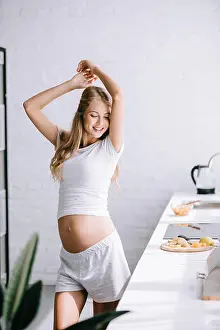 Maternal Prints: smiling beautiful pregnant woman in white clothing standing in kitchen at home