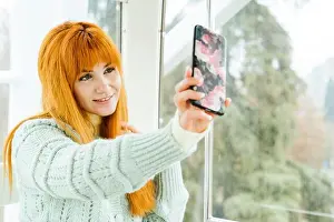 Beautiful Woman Prints: Smiling beautiful woman taking selfie by window