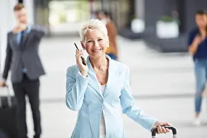 Lobby Prints: Smiling confident blond lady in light blue jacket crossing airport and talking on mobile phone
