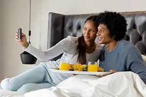 Intimacy Prints: Smiling Diverse couple taking selfie in bedroom