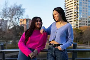Satisfied Prints: Smiling Hispanic female friends in colorful wear standing near pond on street with residential buildings while spending