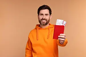 Smiling man showing passport and tickets on beige background