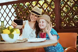 European Culture Prints: smiling modern family with plate of local farm lemons video chatting on a smartphone and having brunch in the terrace