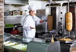 Roast Prints: smiling russian mature man chef wearing uniform cutting meat for kebab on kitchen in fast food restaurant