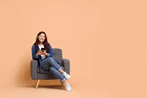 Texting Prints: Smiling woman with smartphone sitting in armchair on beige background. Space for text