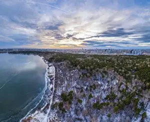 Yekaterinburg Prints: Snow-covered forest on lake shore with the first ice at sunset and the city on horizon