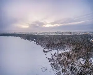 Yekaterinburg Prints: Snow-covered forest on lake shore with ice at sunset and the city on horizon