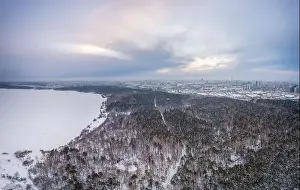 Yekaterinburg Prints: Snow-covered forest on lake shore with ice at sunset and the city on horizon