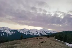 A snowy Carpathian mountain range with a violet sky and clouds in the background