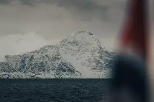 Snowy mountain behind Norwegian flag in the arctic Lyngen Alps in Norway, winter