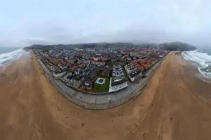Spectacular drone view of powerful foamy ocean rolling on sandy beach near typical red roofed residential buildings