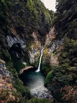 Spectacular drone view of powerful stream of waterfall flowing in lake in mountainous forest