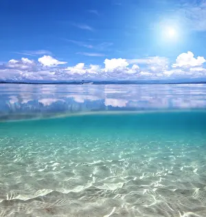 Split Prints: Split view over and under water in the Caribbean sea with clouds reflected on surface and a sandy seabed
