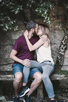 Kissing Prints: Stock photo of a young couple kissing sitting under a tree climbing a wall