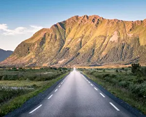 Straight asphalt road with mountain landscape against blue sky in Lofoten, Norway