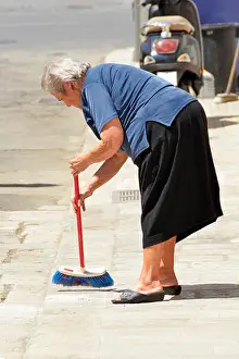 Bending Prints: Street scene old woman senior citizen bending to sweep pavement outside her home in Polignano a Mare town in Province