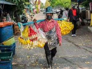 Garlands Prints: A street vendor is carrying garlands of jasmine and marigold flowers on the alley of Khlong Toei Market