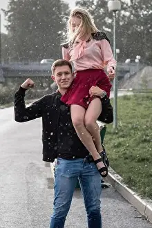 Strong man carrying his woman on shoulder in the street on rain