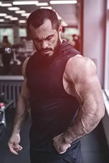 Bodybuilding Prints: strong young bearded caucasian male athlete with big muscles wearing black sportswear in sport fitness gym