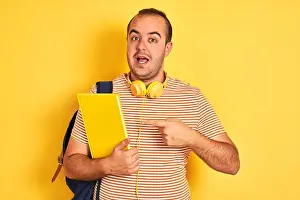 Optimistic Prints: Student man wearing backpack headphones holding notebook over isolated yellow background very happy pointing with hand