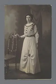1907 Prints: Studio portrait of an unknown woman next to a chair