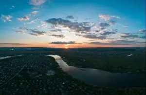 Stunning panoramic aerial view of the natural landscape with lush green meadows, a river and a village at sunset