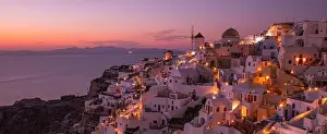 Stunning sunset landscape. Beautiful view of fabulous village of Oia with traditional white houses and windmills in Santorini island at night, Greece