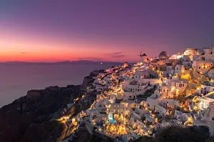 Stunning sunset landscape. Beautiful view of fabulous village of Oia with traditional white houses and windmills in Santorini island at night, Greece