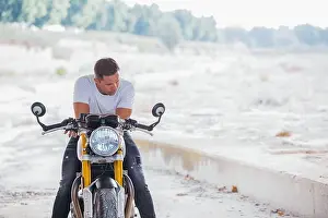 Wall Street Prints: Stylish male biker sitting on modern motorcycle in urban area and looking down