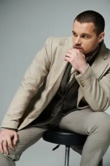 Stool Prints: A stylish man in a beige suit sits on a stool, thoughtfully gazing off to the side