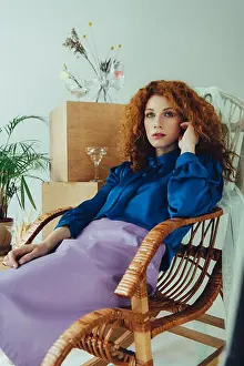 Redhead Prints: stylish redhead girl sitting in wicker chair near wooden boxes and dried flowers on grey