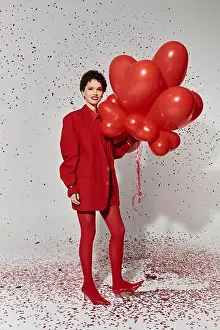 Glam Prints: A stylish woman in red joyfully holds heart shaped balloons amidst confetti