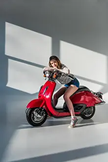 Caucasian Woman Prints: stylish woman in shorts looking at camera while sitting on red scooter